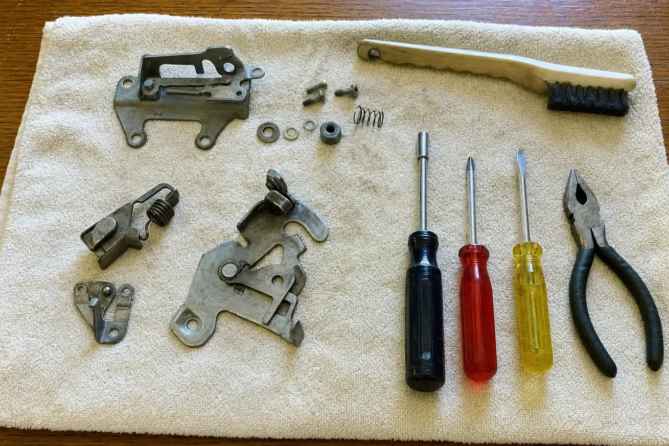 Dismantled door latch — cam plate, spring catch, striker and bracket — laid out with drivers and pliers